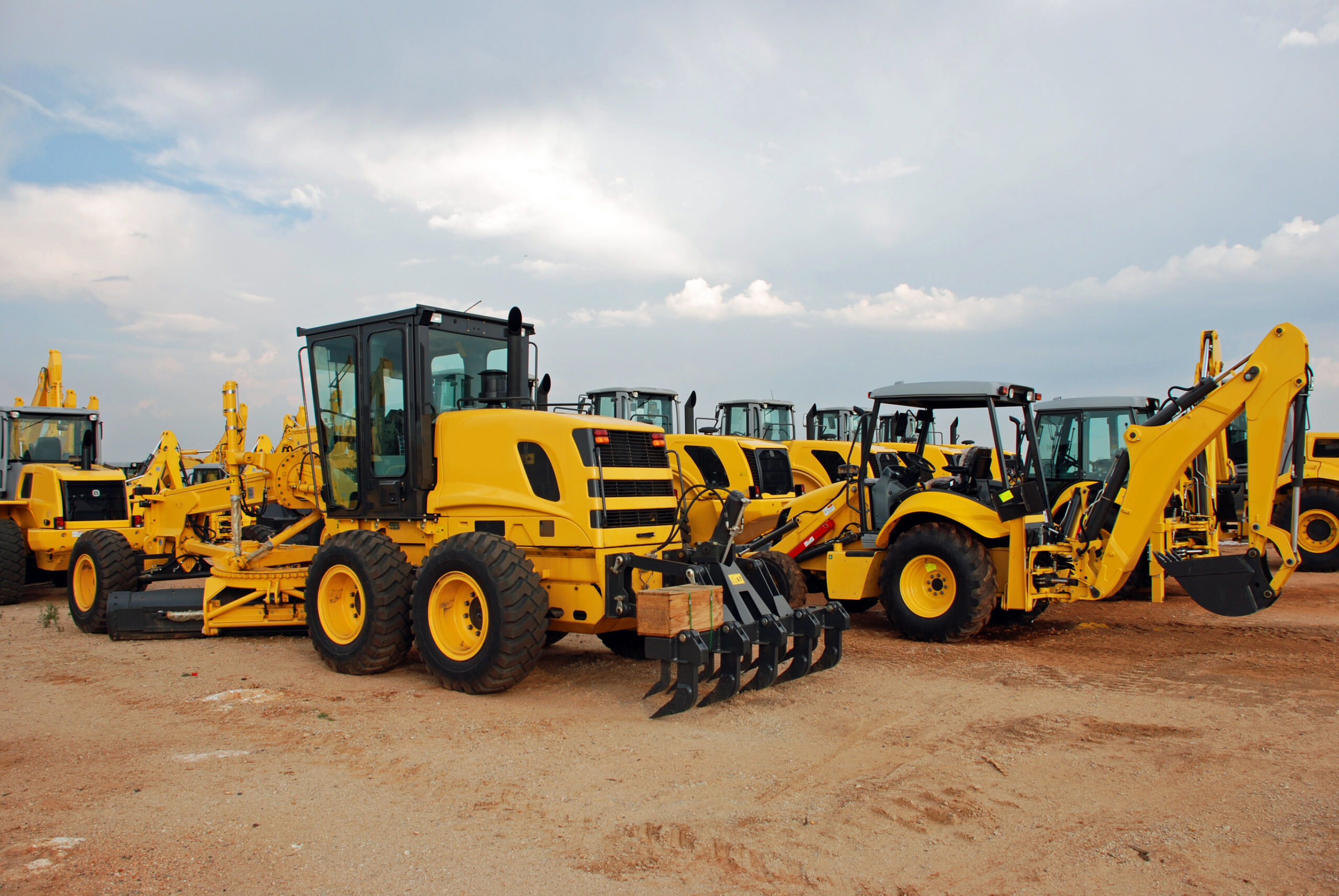 image of various construction vehciles parked in a line in a dirt parking lot
